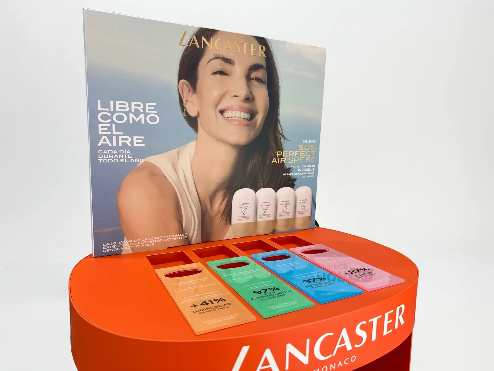 Présentoir de comptoir Lancaster Sun Perfect Air : plateau ovale orange avec quatre languettes en plexiglas de couleur, chacune portant sa promesse d'efficacité